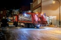 Garbage collecting truck moves along city street. Dark time of day. Royalty Free Stock Photo