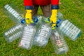 Hands in yellow gloves holding big empty plastic bottles. Grass on a background