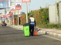 a garbageman worker in protective clothing walking with a dustbin collecting garbage for trash removal