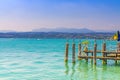 Garda lake with blue azure turquoise water and wooden pier dock, coast with mountain range Royalty Free Stock Photo