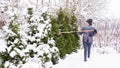 The garden is abundantly covered with snow. The gardener uses a broom to shake off snow from the branches of conifers so that they