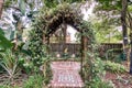 Garden archway overed with green folage onto red brick patio