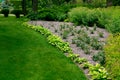 Garden bed with bushes near meadow turf lawn and flower bed with growth roses.