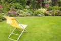 Garden chair on a green grass in a beautiful flower garden