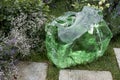 The garden decoration with artificial stone made of green transparent glass among flowers