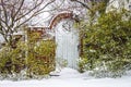 Garden gate in the snow - Wooden with octogan cutout in brick fence with arch and green bushes but bare winter branches behind Royalty Free Stock Photo