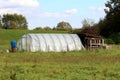 Garden greenhouse made of metal pipes and transparent nylon next to vintage retro homemade temporary wooden rabbit cages Royalty Free Stock Photo