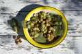 Garden hazelnut with green leaves in a yellow cup on a white wooden background flat top view