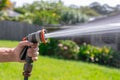 Garden hose with nozzle. Man\'s hand holding spray gun and watering plants, spraying water on grass in backyard Royalty Free Stock Photo