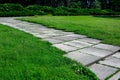 Garden path made of square tiles overgrown with grass in a park with a green lawn. Royalty Free Stock Photo