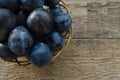 Garden plums in a wicker basket on a wooden background.