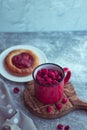 In the foreground is a red mug with garden raspberries, in the background a cheesecake with berry filling, light background, defoc