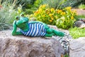 A garden sculpture of a frog lying on the floor reading a book