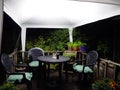 Garden seating area covered by a white gazebo at night lit by bright white light with pot plants and decking Royalty Free Stock Photo