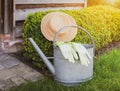 Gardening concept: Summer hat, zinc watering can and garden gloves at Boxwood plant in the garden.