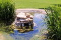 Garden water feature made with natural rocks with lush lawn and tall water grass Royalty Free Stock Photo