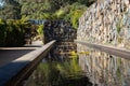 Garden water pond feature with rock feature wall, water lilies, arch doorway along stone walkway surrounded by trees Royalty Free Stock Photo