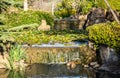 Garden water pond filled with Lillies, waterfalls over sandstone rock ledge set in lush plants surrounds Royalty Free Stock Photo