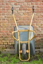 Garden wheelbarrow leaning against a red brick wall in a home backyard. Landscaping equipment and tools to carry and