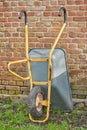 Garden wheelbarrow leaning against a red brick wall in a home backyard. Landscaping equipment and tools to carry and