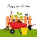 A garden wheelbarrow with a plant and tools on the background of a fence and grass. The concept of growing your garden, caring for Royalty Free Stock Photo