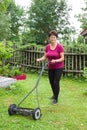 Happy smiling senior woman mowing grass with lawn mower in the garden Royalty Free Stock Photo