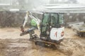 Garden worker in the small digger continues to work even in heavy rain Royalty Free Stock Photo