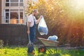 The gardener collects the bags of leaves and puts them in the cart. The sun shines brightly on the right side