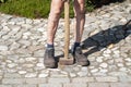 a gardener in dirty work clothes and boots holds a two-bladed iron hammer Royalty Free Stock Photo