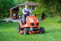 Gardener driving a riding lawn mower in garden