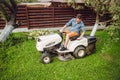 Gardener driving a riding lawn mower in a garden. Royalty Free Stock Photo