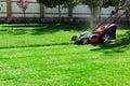 Gardener by electric lawn mower cutting green grass in the garden. Garden meadow lawn cutting. Worker guy trimmed grass field. Royalty Free Stock Photo