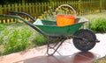 Gardener green wheel barrow with orange pail Royalty Free Stock Photo