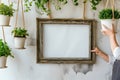 gardener hangs an empty rustic frame on a wall beside indoor hanging planters