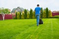 A gardener with a lawn mower is cutting grass in the garden in the house backyard Royalty Free Stock Photo