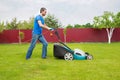 A gardener with a lawn mower is cutting green grass in the garden in the house backyard Royalty Free Stock Photo