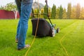 A gardener with a lawn mower is cutting green grass in the garden, in the house backyard on a sunny summer day. The legs of the Royalty Free Stock Photo