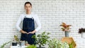 Gardener looked discreet in white T-shirt. Denim apron, look at the camera background white brick wall. Presenter air filter trees