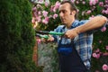 Gardener man in blue work uniform, holding pruner and cutting a hedge in the garden. Home and garden decoration concept Royalty Free Stock Photo