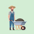 Gardener man pushing wheelbarrow full of earth compost male farmer working in garden wearing overalls gardening concept