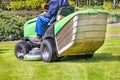 A gardener mows a green lawn while riding a tractor lawn mower on a bright spring day Royalty Free Stock Photo