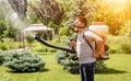 Gardener in protective mask and glasses spraying toxic pesticides trees