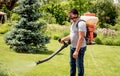 Gardener in protective mask and glasses spraying toxic pesticides trees