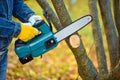 A gardener pruns trees with a lightweight cordless chain saw. Work in the autumn garden Royalty Free Stock Photo