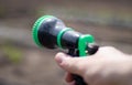 The gardener`s hand holds a hose with a sprayer and waters the plants in the garden. Green atomizer in hand with a large lan. Royalty Free Stock Photo