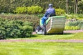 A gardener takes care of a green lawn, cutting the grass on a tractor lawn mower on a bright spring day Royalty Free Stock Photo