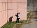 A gardener trims the grass on a sidewalk with a weed eater. He wears all the prescribed safety clothes