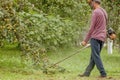 Gardener using machine cutting green grass in garden. Garden equipment. Young man mowing the grass with a trimmer Royalty Free Stock Photo