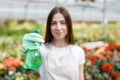 Gardening concept. Pretty smiling woman in apron holding sprayer in hand and looking to camera, standing in modern greenhouse on Royalty Free Stock Photo