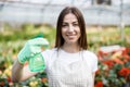 Gardening concept. Pretty smiling woman in apron holding sprayer in hand and looking to camera, standing in modern greenhouse on Royalty Free Stock Photo